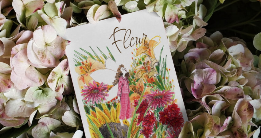 Photo of a birth announcement card. The card contains a drawing of a little girl in her dream world, flying like a fairy and surrounded by colourful flowers.